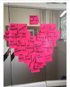 pink post it notes are hanging on the wall in front of a mirror that has been decorated with writing