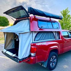 a red pick up truck parked in a parking lot with a tent on the back