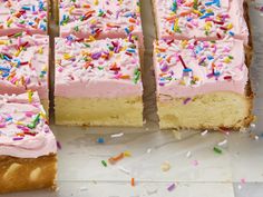 a cake with pink frosting and sprinkles cut into squares