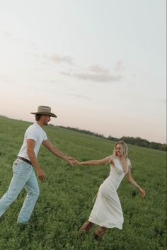 a man and woman are holding hands in the middle of a grassy field at sunset