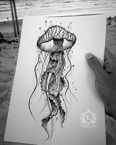 a person holding up a drawing of a jellyfish in front of the ocean and beach