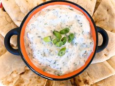 an orange bowl filled with white dip surrounded by pita chips