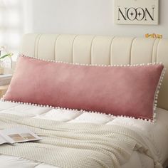 a bed with a pink pillow on top of it next to a white headboard