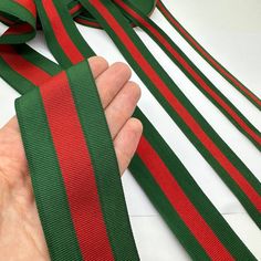 a hand is holding a red and green striped tie with two long ties on it