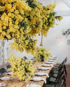 the table is set with white plates and place settings, along with yellow flowers in vases