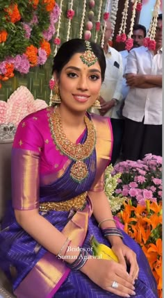 a woman in a purple and gold sari sitting on a bench next to flowers