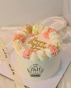 a white cake with pink and gold frosting on top, sitting on a napkin next to a knife