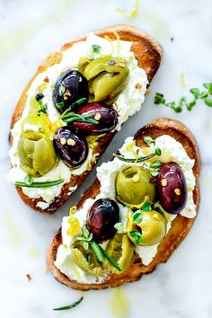 two pieces of bread with olives and whipped cream on top, sitting on a marble surface