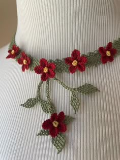 a woman wearing a white top with red flowers on it's neck and green leaves