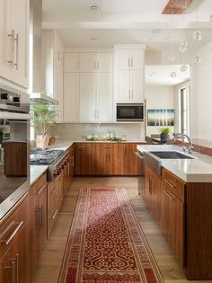 a kitchen with white cabinets and wooden floors is seen in this image, along with a red rug on the floor