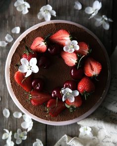 a chocolate cake with strawberries and cherries on top, surrounded by white flowers