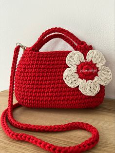 a red crocheted purse with a flower on the front and side, sitting on a wooden table