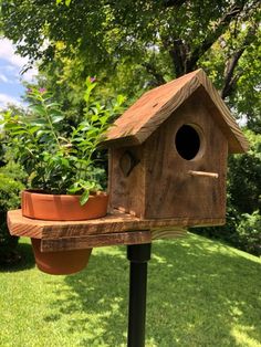 a wooden bird house sitting on top of a pole next to a potted plant