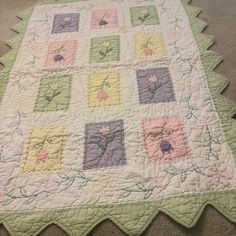 a quilt on the floor is made with squares and flowers in pastel colors,