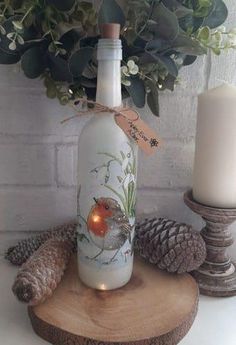 a bottle with a bird on it sitting next to a candle and some pine cones