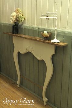 an old table is painted white and has some flowers on the shelf next to it