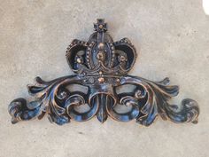 an ornate metal wall hanging on the side of a cement wall with a crown design