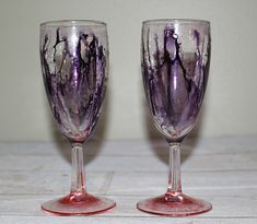 two wine glasses sitting next to each other on top of a wooden table covered in purple and white paint