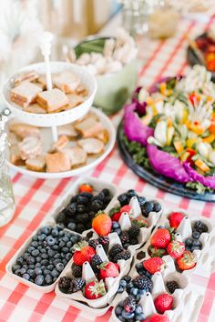 a table topped with trays of food and plates filled with berries, blueberries, strawberries