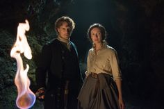 a man and woman standing next to each other in front of a fire pit at night