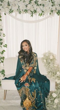 a woman in a green dress sitting on a white couch next to a flower covered wall