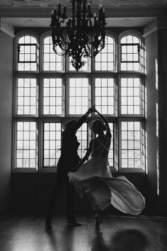 a man and woman dancing in front of a window with chandelier hanging from the ceiling