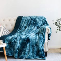 a blue blanket sitting on top of a white couch next to a potted plant