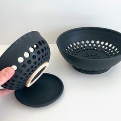 a person is holding a black strainer over a white table with two plates on it