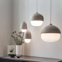 three lamps hanging from the ceiling above a table with flowers in vases on it