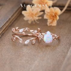 a white opal and diamond ring sitting on top of a wooden table next to flowers