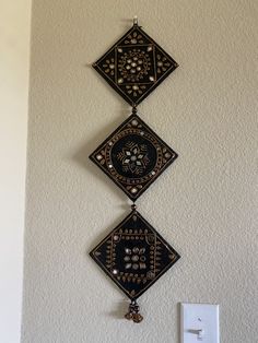 two decorative wall hangings on the side of a white wall next to a light switch