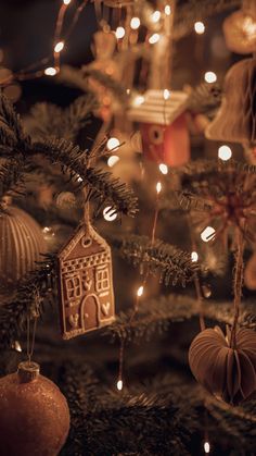 ornaments are hanging on the christmas tree with lights in the background and an ornament that looks like a gingerbread house