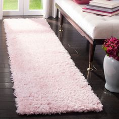 a pink rug is on the floor in front of a white bench and window with flowers