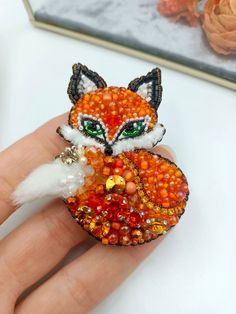 a hand holding a ring with an orange fox on it's face and green eyes