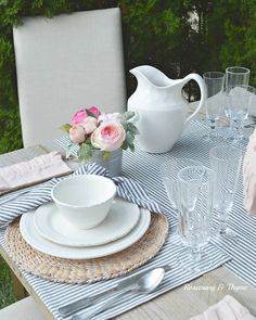 the table is set with white dishes and pink flowers