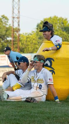 some baseball players are sitting on the grass and one is talking on his cell phone