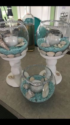 two glass bowls filled with sand and sea shells on top of a stone countertop