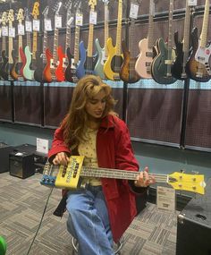 a woman sitting on the floor playing an electric bass guitar in front of several guitars