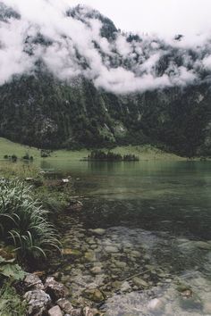 a lake surrounded by mountains and clouds in the sky