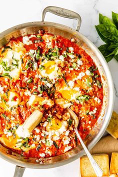 a pizza with cheese and spinach on top in a skillet next to bread