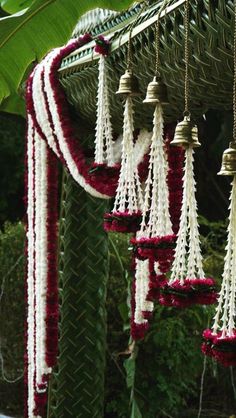 several bells hanging from the ceiling with red and white flowers on them in front of a green plant