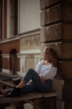 a woman is sitting on the ledge of an old building and looking off into the distance