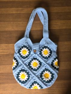 This handbag/tote bag is made with daisy Granny squares and a crocheted handle.  The squares are made with Hobby Lobby I love this yarn in the colors white, yellow, blue spruce and soft blue.  The primary color of the bag is soft blue.  The bag is lined in beige and contains one zippered pocket.  The bag has a single button closure. Blue Crochet Bag With Granny Square For Everyday, Blue Square Crochet Bags, Blue Hand Knitted Rectangular Bag, Hand Knitted Blue Rectangular Shoulder Bag, Blue Hand Knitted Rectangular Shoulder Bag, Blue Granny Square Rectangular Shoulder Bag, Blue Granny Square Shoulder Bag For Daily Use, Blue Granny Square Shoulder Bag For Everyday, Blue Square Crochet Bag