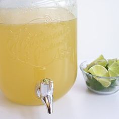 a glass jar filled with liquid next to a bowl of limes and a spoon