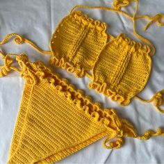 two crocheted bikinisuits are laying on a white sheet and one is yellow