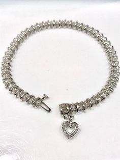 "Diamond Tennis Bracelet with Brilliant Cut Diamonds in Dot and Dash style setting in 14K White Gold with Total Weight of Diamonds approximately 1.25 Carats. Diamond heart is free moving and dangling at the clasp of the bracelet. Brilliant cut diamonds are channel set. Diamonds are approximately G/H Color and SI Clarity. Bracelet is handmade, each link moving with a tongue and groove lock and safety catch. Bracelet is 7.25\" long. Can be shortened. Client keeps extra links when shortened. Apprai Formal White Gold Heart Tennis Bracelet, Elegant Heart-shaped Sterling Silver Bracelet For Formal Occasions, Elegant White Gold Heart Tennis Bracelet, Elegant White Gold Heart-shaped Tennis Bracelet, Diamond Heart-shaped Jubilee Bracelet, Classic Heart Jubilee Bracelet For Anniversary, Classic Jubilee Heart Bracelet For Anniversary, White Gold Heart Cut Bracelet Fine Jewelry, Diamond Heart Cut Jubilee Bracelet