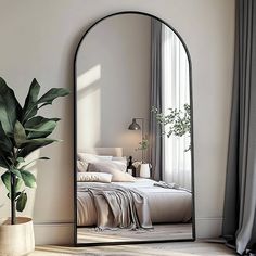 a large mirror sitting next to a bed in a room with a plant on the floor