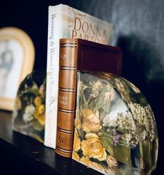 two books are sitting on a shelf next to a glass vase with flowers in it