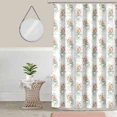 a white shower curtain with pink flowers on it and a mirror hanging above the shower