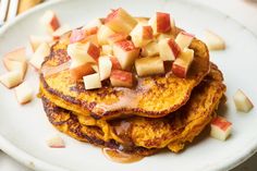 a stack of pancakes topped with apples on top of a white plate next to silverware